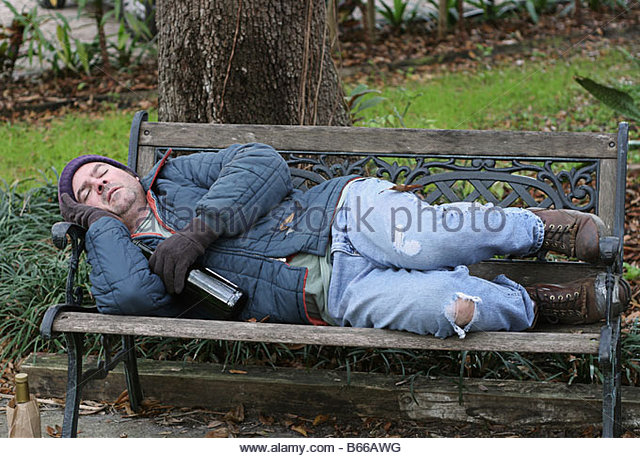 a-full-view-of-a-homeless-man-asleep-on-a-park-bench-with-his-wine-b66awg.jpg