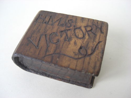 A piece of carved wood in the shape of a book. It is inscribed HMS Victory and would have been...